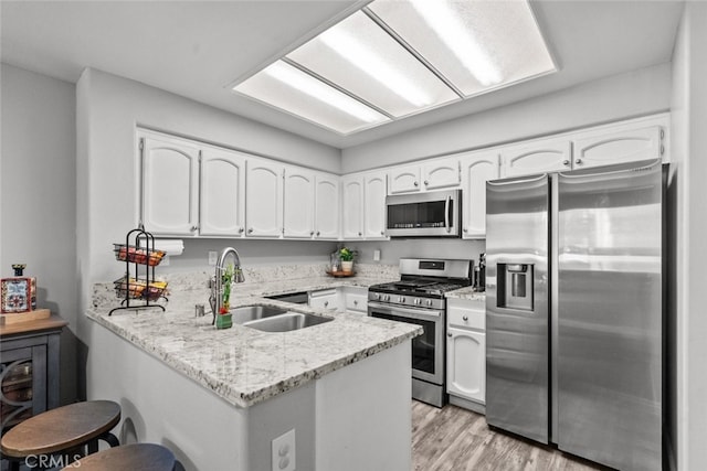 kitchen with kitchen peninsula, sink, white cabinets, light wood-type flooring, and appliances with stainless steel finishes