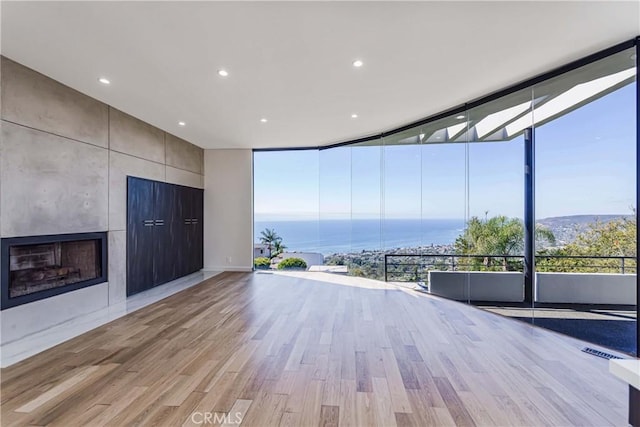 unfurnished living room with expansive windows, a water view, light wood-type flooring, and a fireplace