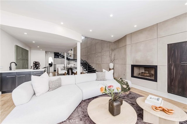 living room with a large fireplace, sink, light hardwood / wood-style floors, and tile walls