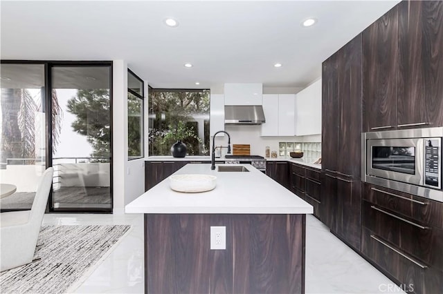 kitchen with stainless steel microwave, a kitchen island with sink, exhaust hood, and white cabinets