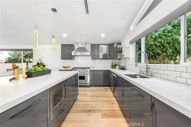 kitchen featuring appliances with stainless steel finishes, pendant lighting, sink, gray cabinetry, and wall chimney exhaust hood