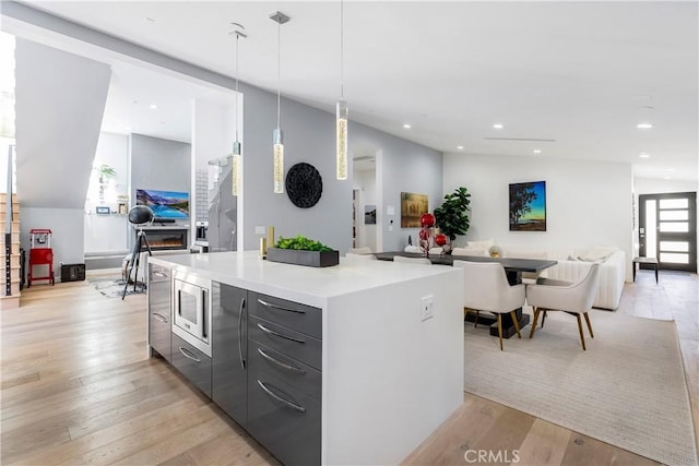 kitchen with pendant lighting, lofted ceiling, light hardwood / wood-style flooring, stainless steel microwave, and a center island with sink