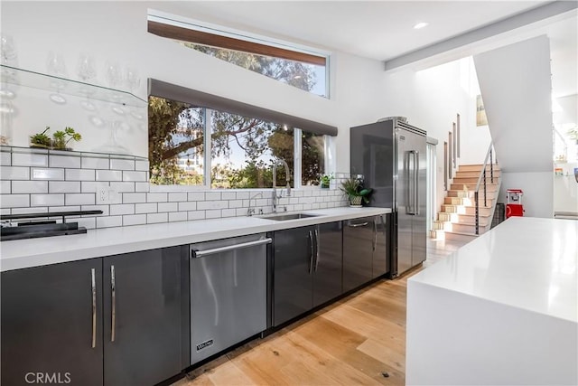 kitchen with tasteful backsplash, appliances with stainless steel finishes, sink, and light hardwood / wood-style floors