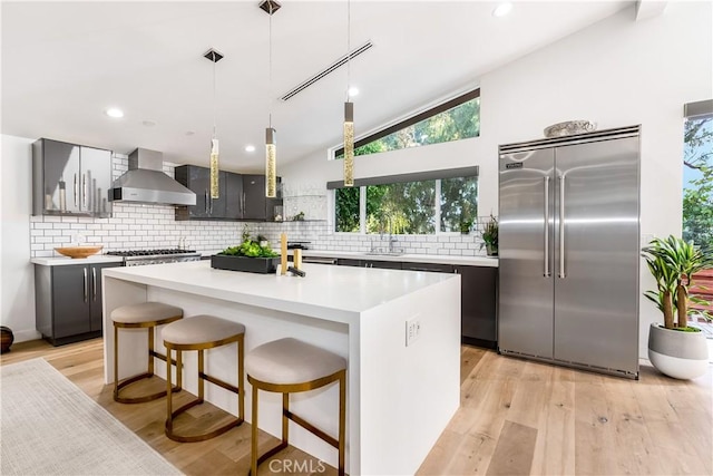 kitchen featuring a kitchen island, stainless steel built in refrigerator, sink, hanging light fixtures, and wall chimney exhaust hood