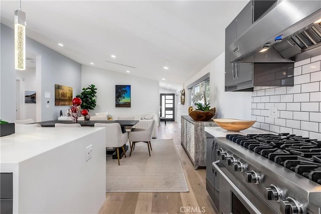 kitchen with stainless steel stove, hanging light fixtures, range hood, vaulted ceiling, and light wood-type flooring