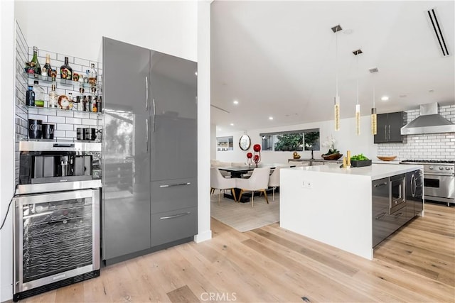 kitchen featuring built in appliances, hanging light fixtures, a kitchen island, beverage cooler, and wall chimney range hood