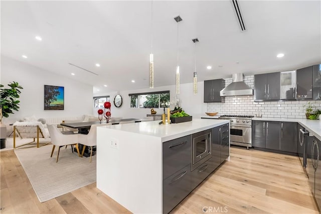 kitchen with stainless steel appliances, a kitchen island, wall chimney range hood, and decorative light fixtures