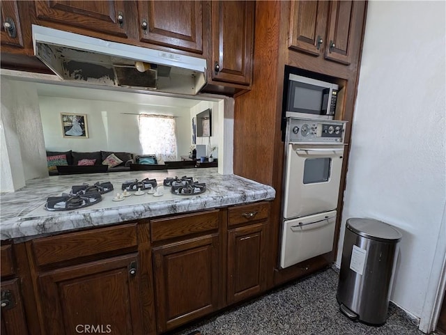 kitchen with dark brown cabinets, light stone counters, and white appliances