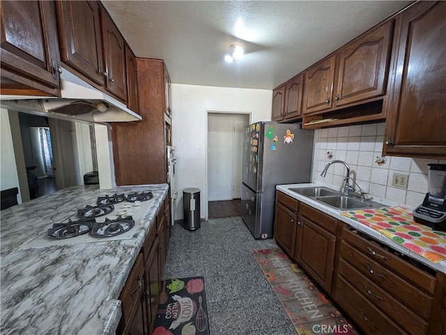 kitchen featuring white gas cooktop, backsplash, sink, dark brown cabinets, and stainless steel refrigerator