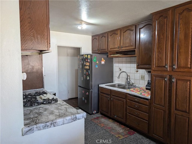 kitchen featuring stainless steel refrigerator, dark brown cabinetry, sink, white gas cooktop, and backsplash