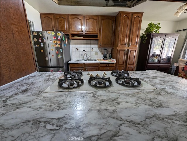 kitchen featuring backsplash, white gas stovetop, sink, and stainless steel refrigerator