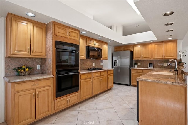 kitchen featuring sink, light tile patterned floors, light stone counters, black appliances, and a raised ceiling