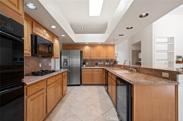 kitchen with sink, beverage cooler, black appliances, a raised ceiling, and light stone countertops