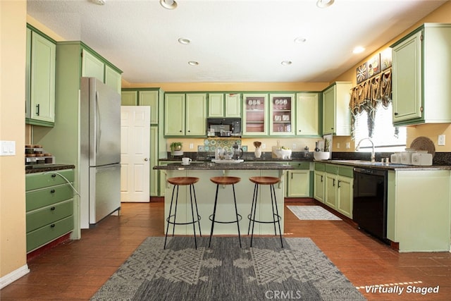 kitchen with a center island, black appliances, a kitchen bar, sink, and green cabinets