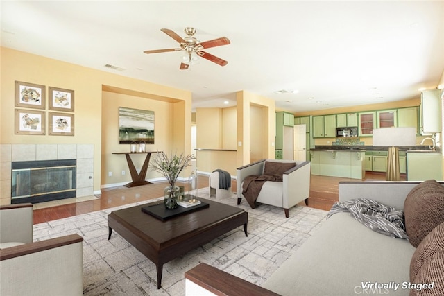 living room featuring light wood-type flooring, ceiling fan, a fireplace, and sink