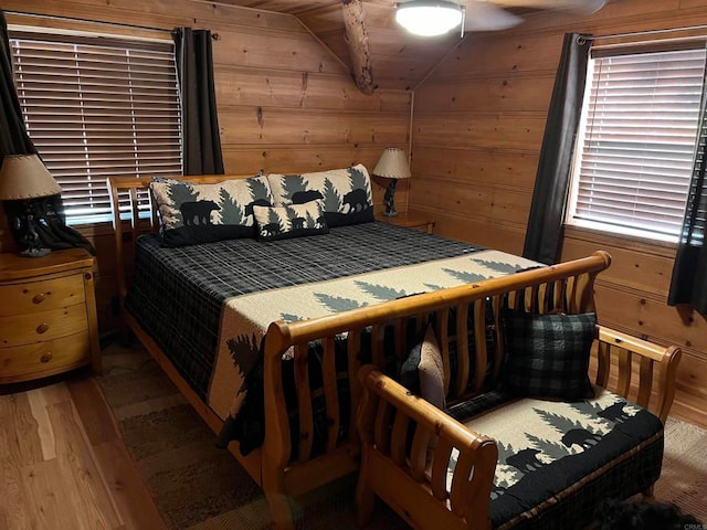 bedroom featuring wooden walls, vaulted ceiling, hardwood / wood-style flooring, and ceiling fan