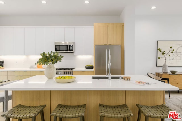 kitchen featuring a kitchen breakfast bar, white cabinetry, stainless steel appliances, and an island with sink