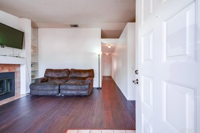 living room featuring a textured ceiling, a tiled fireplace, dark wood-type flooring, and built in features