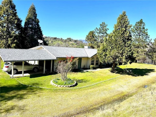 view of front facade featuring an attached carport, a front yard, and roof with shingles