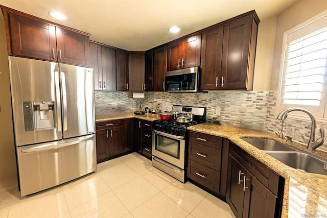 kitchen featuring tasteful backsplash, light stone countertops, sink, dark brown cabinetry, and stainless steel appliances