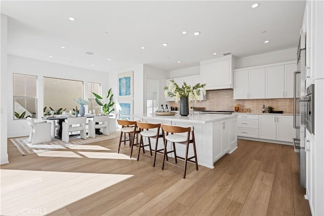 kitchen with a breakfast bar, white cabinetry, an island with sink, and light hardwood / wood-style flooring