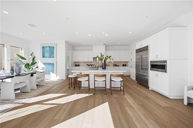 kitchen with a kitchen breakfast bar, stainless steel appliances, light hardwood / wood-style floors, white cabinetry, and an island with sink