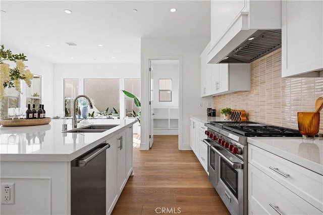 kitchen with white cabinets, custom range hood, light hardwood / wood-style flooring, and appliances with stainless steel finishes