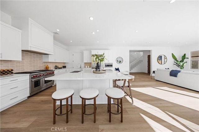 kitchen featuring a center island with sink, double oven range, sink, and light hardwood / wood-style flooring