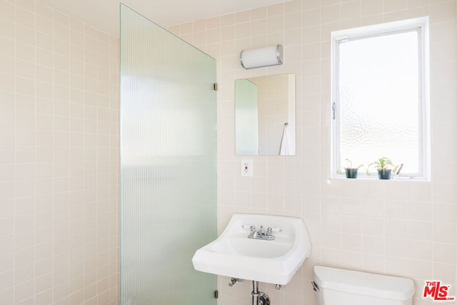 bathroom with toilet, sink, and tile walls