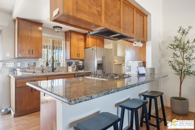 kitchen featuring kitchen peninsula, dark stone counters, sink, light wood-type flooring, and appliances with stainless steel finishes