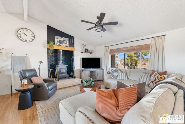 living room with a wood stove, lofted ceiling with beams, light wood-type flooring, a textured ceiling, and ceiling fan