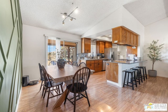 dining room featuring light hardwood / wood-style flooring, a textured ceiling, and vaulted ceiling