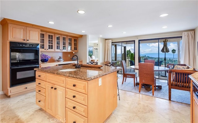 kitchen with sink, stone counters, a center island with sink, black double oven, and a kitchen bar