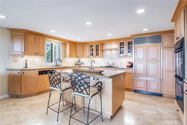 kitchen with a breakfast bar, sink, light stone countertops, a kitchen island with sink, and black appliances