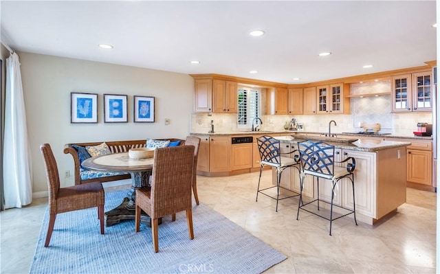 kitchen featuring light brown cabinetry, sink, light stone countertops, and a center island with sink