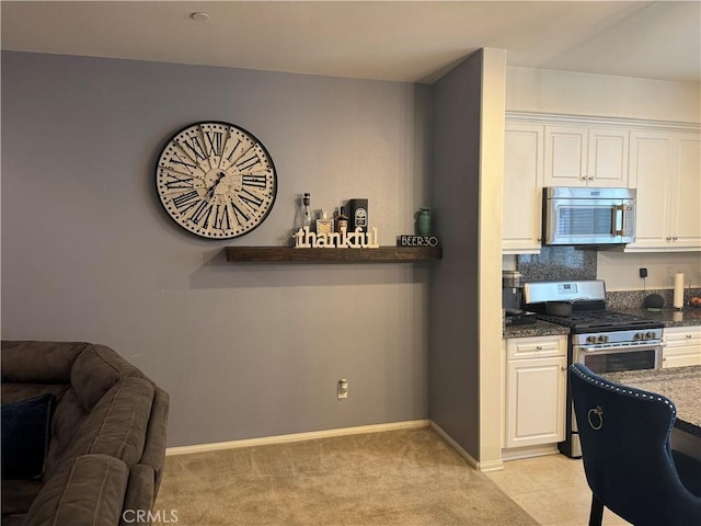 kitchen with dark stone countertops, light colored carpet, white cabinetry, and stainless steel appliances