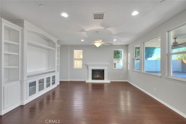 unfurnished living room with built in features, ceiling fan, and dark wood-type flooring