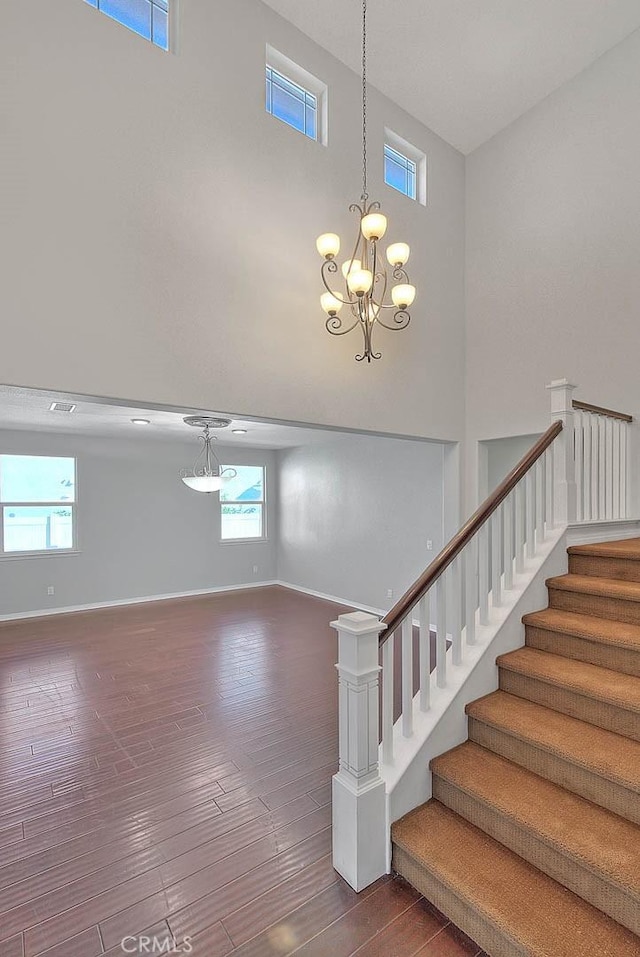 staircase with hardwood / wood-style floors, plenty of natural light, a towering ceiling, and a notable chandelier