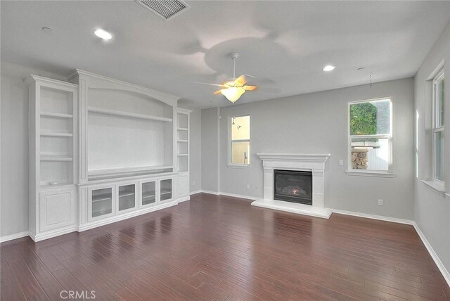 unfurnished living room featuring ceiling fan, built in features, and dark wood-type flooring