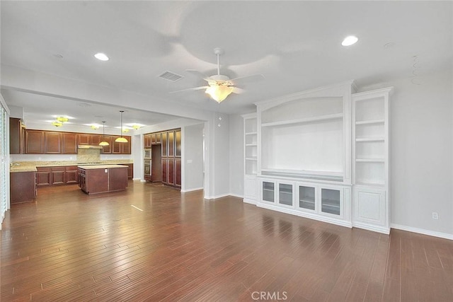 unfurnished living room featuring built in features, ceiling fan, and dark wood-type flooring