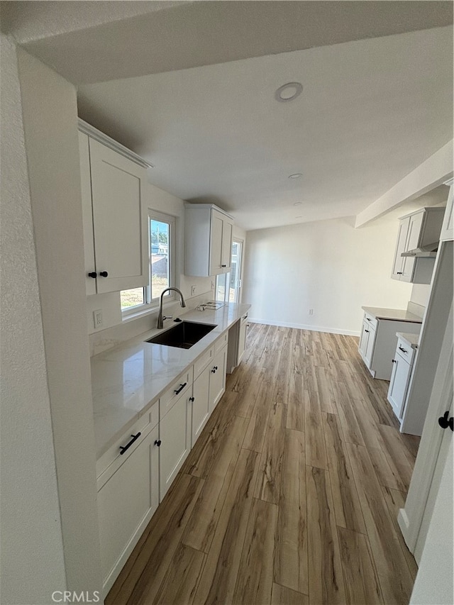 kitchen featuring light stone countertops, sink, light wood-type flooring, and white cabinets