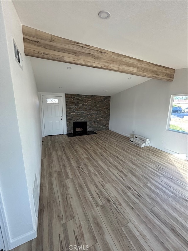 unfurnished living room featuring a stone fireplace, light hardwood / wood-style flooring, and vaulted ceiling with beams