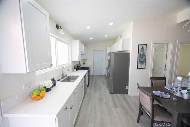 kitchen featuring stainless steel appliances, vaulted ceiling, sink, light hardwood / wood-style flooring, and white cabinets