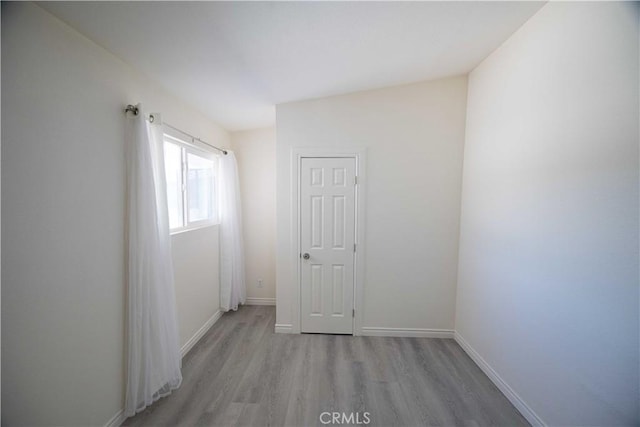 spare room featuring lofted ceiling and light hardwood / wood-style flooring