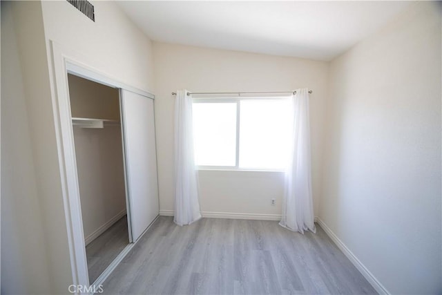 unfurnished bedroom featuring light hardwood / wood-style floors, a closet, and lofted ceiling