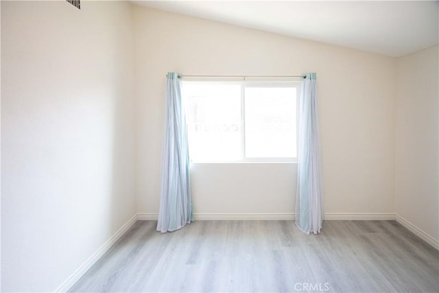 spare room with lofted ceiling and light wood-type flooring