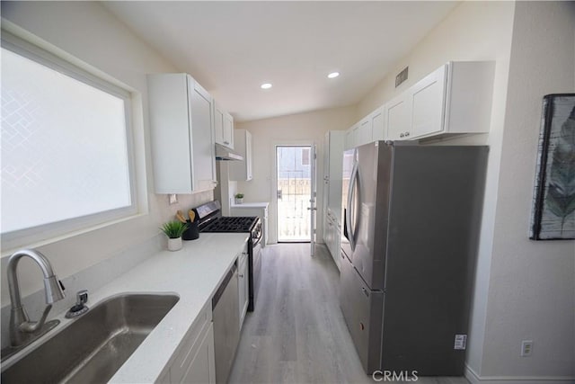 kitchen with sink, light hardwood / wood-style flooring, vaulted ceiling, appliances with stainless steel finishes, and white cabinetry