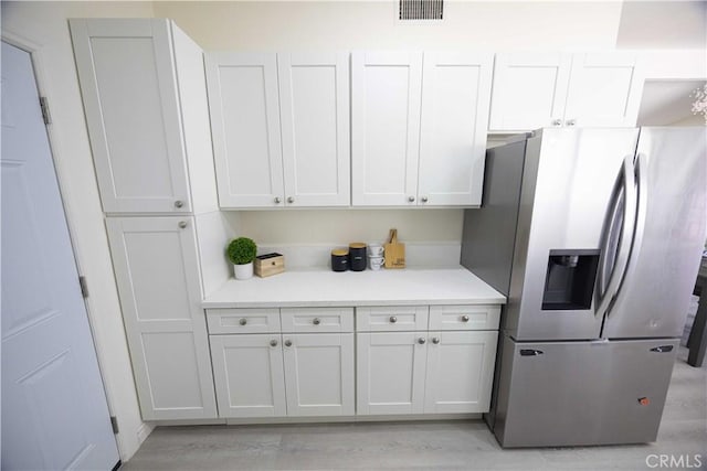 kitchen with stainless steel refrigerator with ice dispenser, light hardwood / wood-style flooring, and white cabinetry