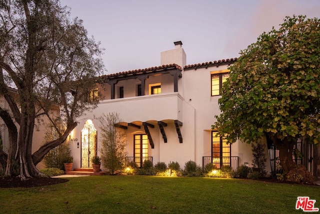 view of front of property featuring a lawn and a balcony