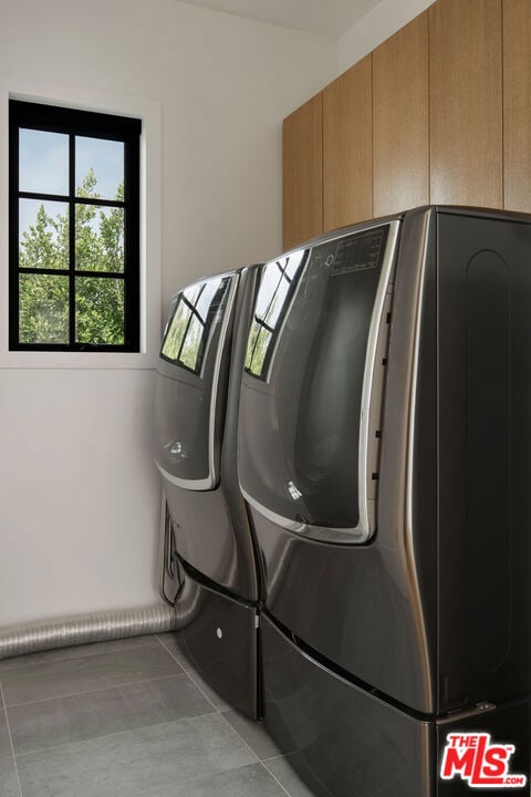 clothes washing area featuring cabinets, light tile patterned floors, and washing machine and clothes dryer